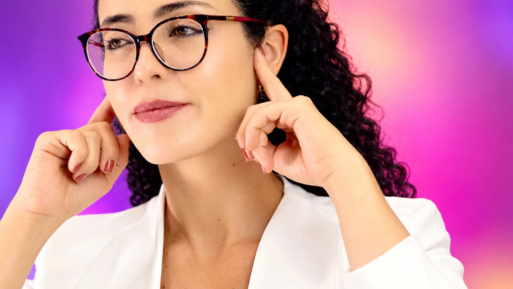 Mulher de óculos aponta para os ouvidos em imagem sobre deficiência auditiva